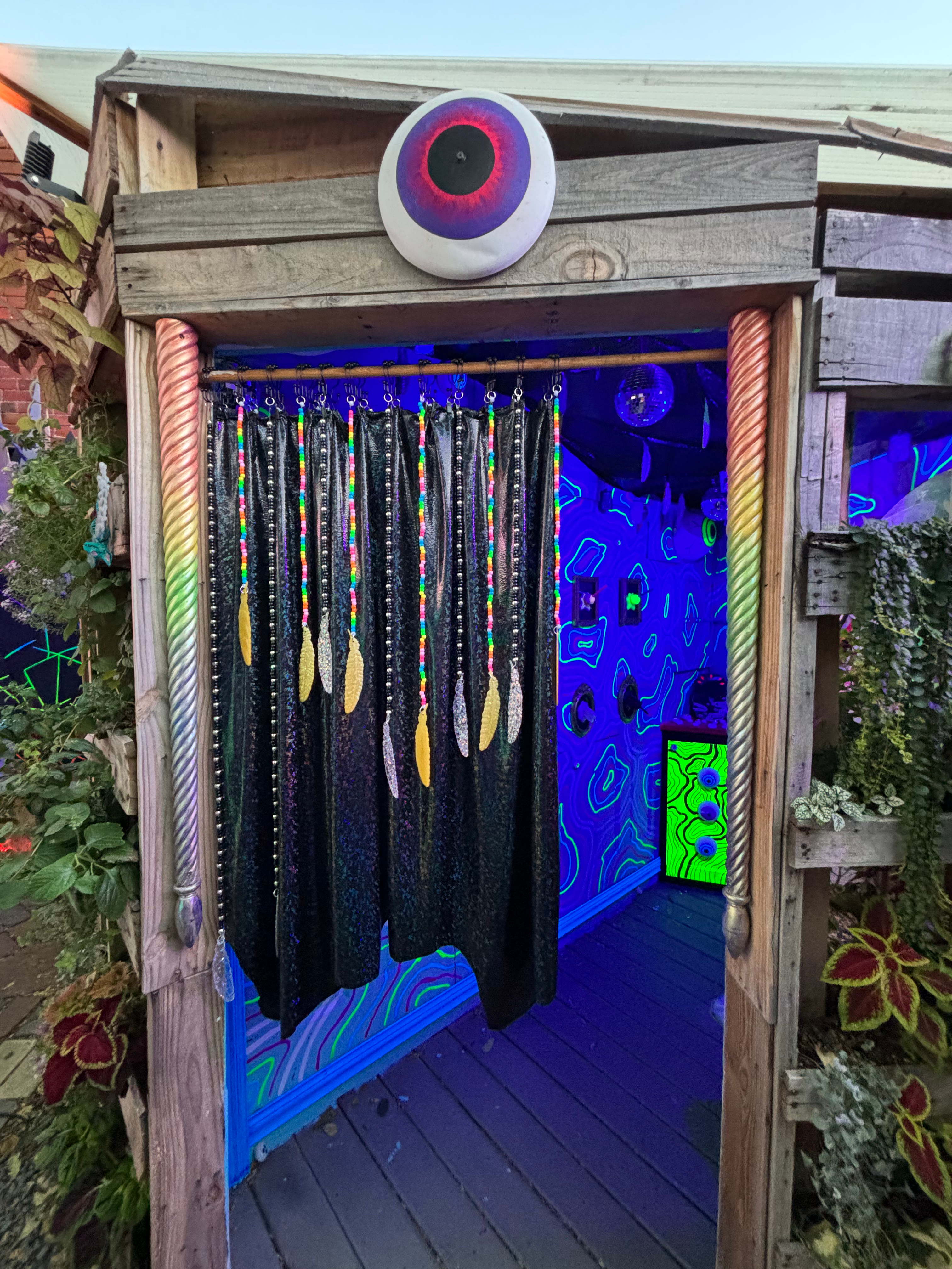 A psychedelic installation featuring a large eyeball sculpture and a beaded curtain, illuminated by UV light.