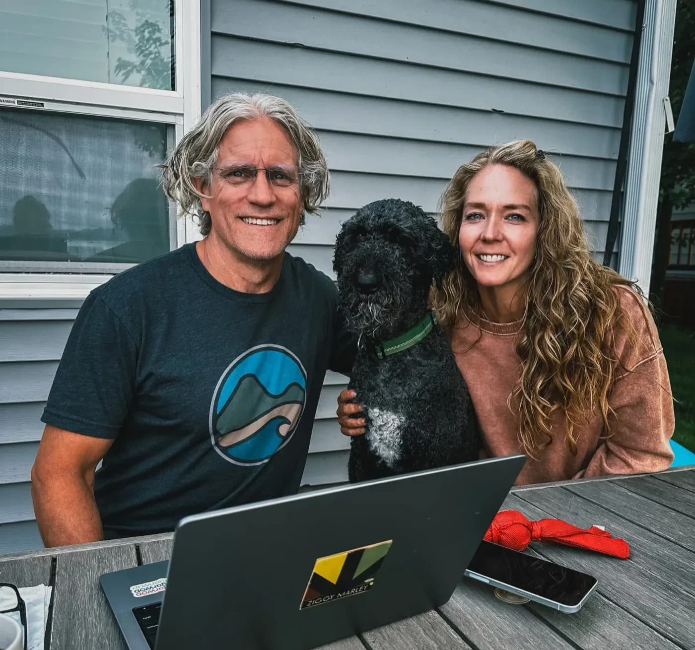 Drew and Shayna Larsen at a laptop on their back deck, with their dog between them