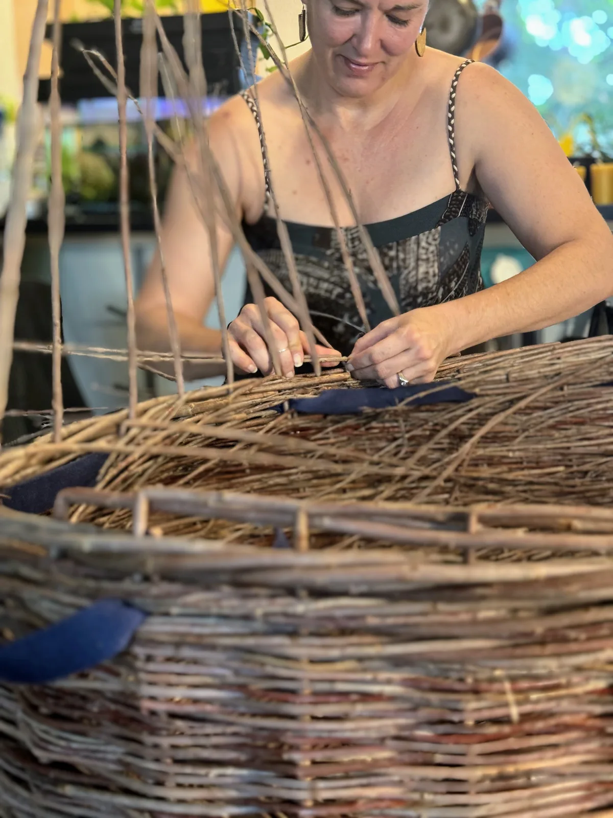 An artist weaves a large basket made of natural fibers in a furnished room.