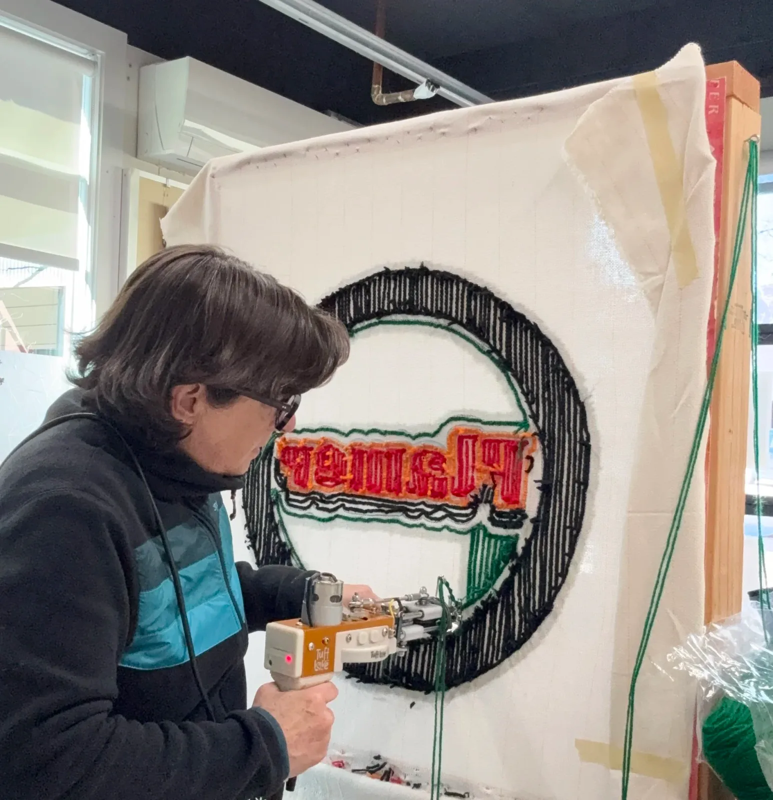 Artist tufting a circular textile artwork with colorful text in progress.
