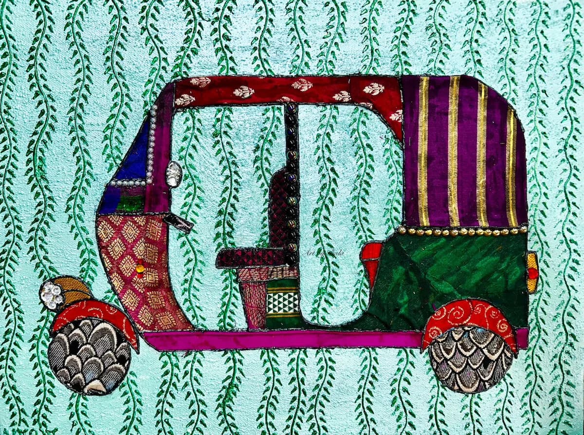 A folk art textile applique of a colorful auto-rickshaw against a light blue vine-patterned background.