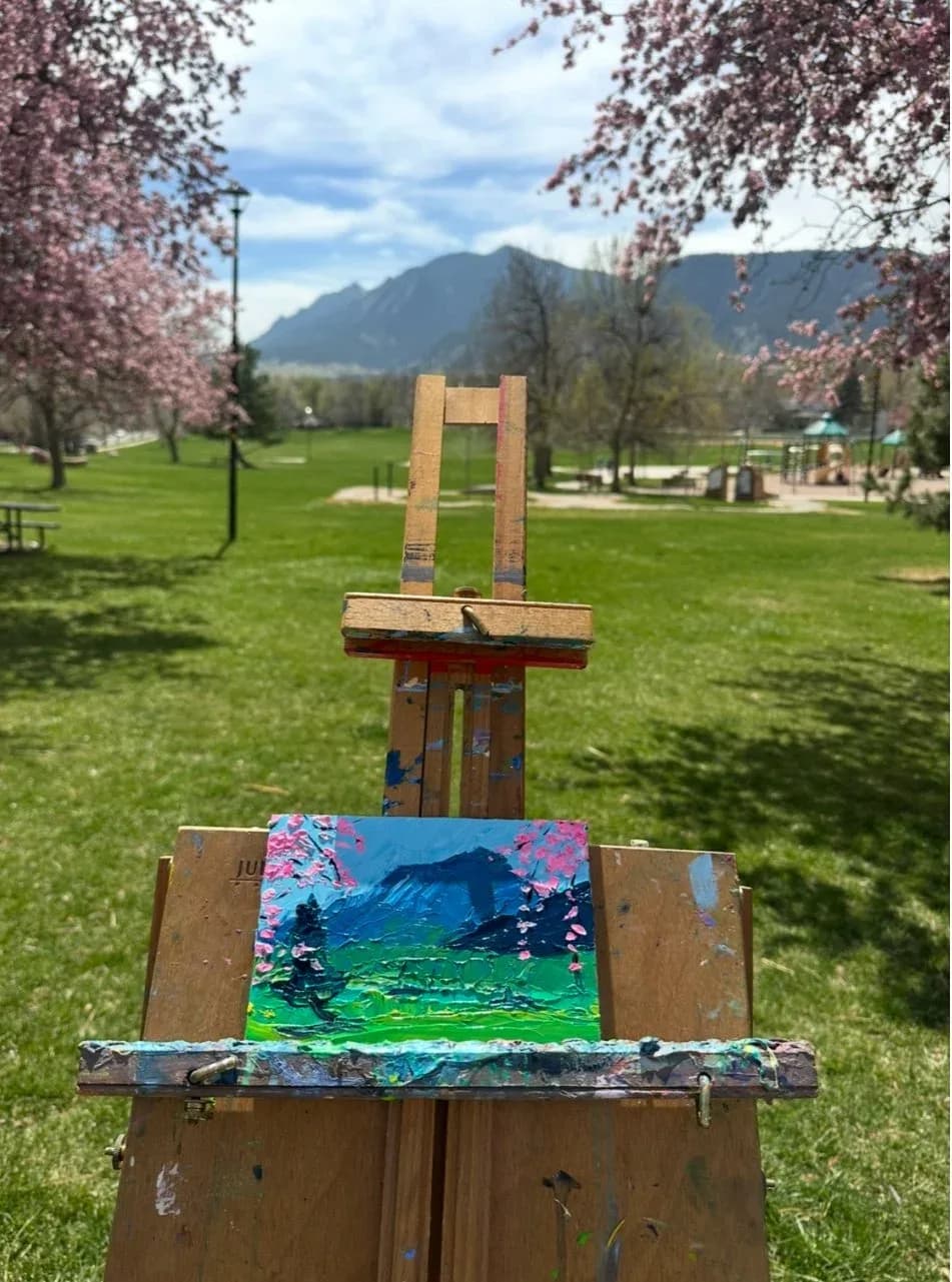 An impressionistic oil painting of the Flatirons mountains with blooming trees in a park setting.