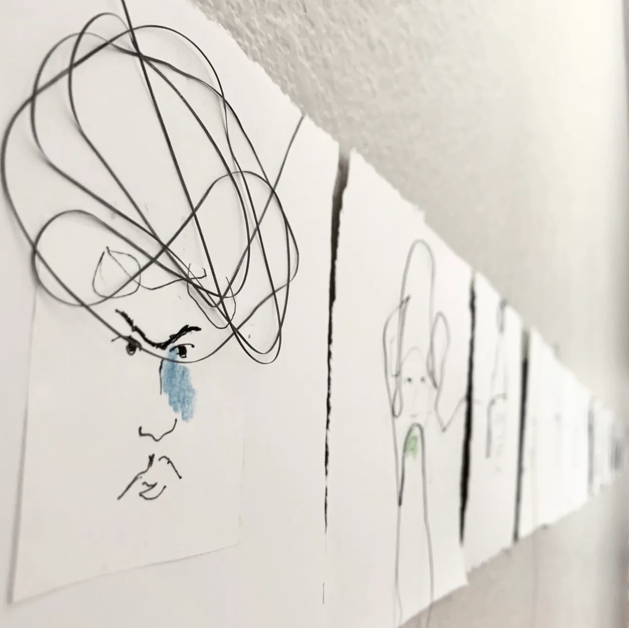 A series of ink drawings of faces, some with blue accents, are displayed in a line.