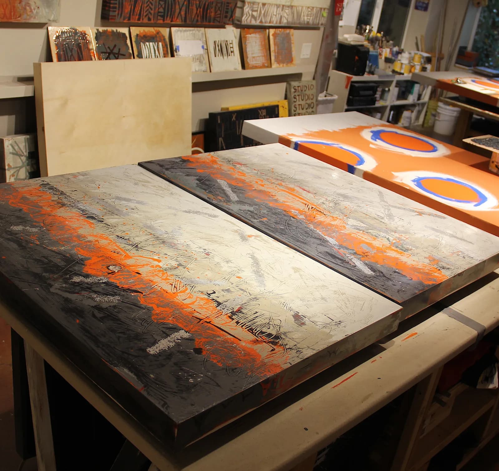 Abstract paintings in progress with orange and gray tones in a studio setting.
