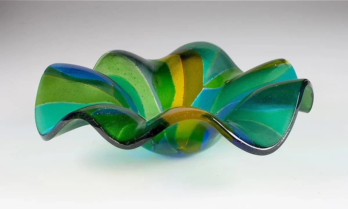 An abstract art glass bowl with swirling green, blue, and yellow hues.