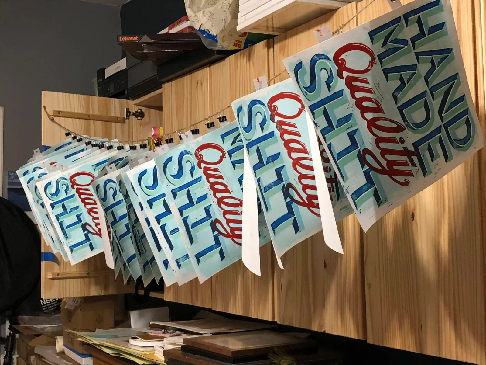 Multiple prints of "Hand Made Quality Shit" hang to dry in a studio.