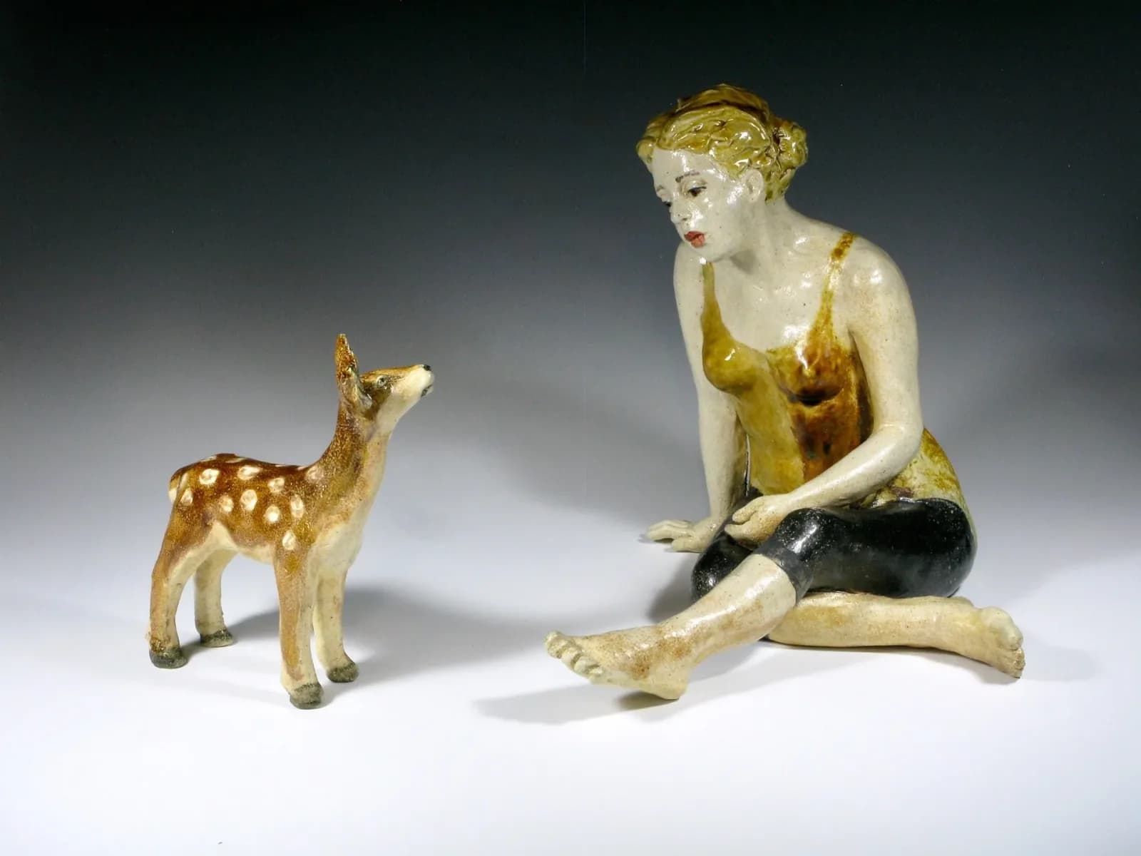 A ceramic sculpture depicts a woman and a fawn in a contemplative pose, rendered in earthy tones.