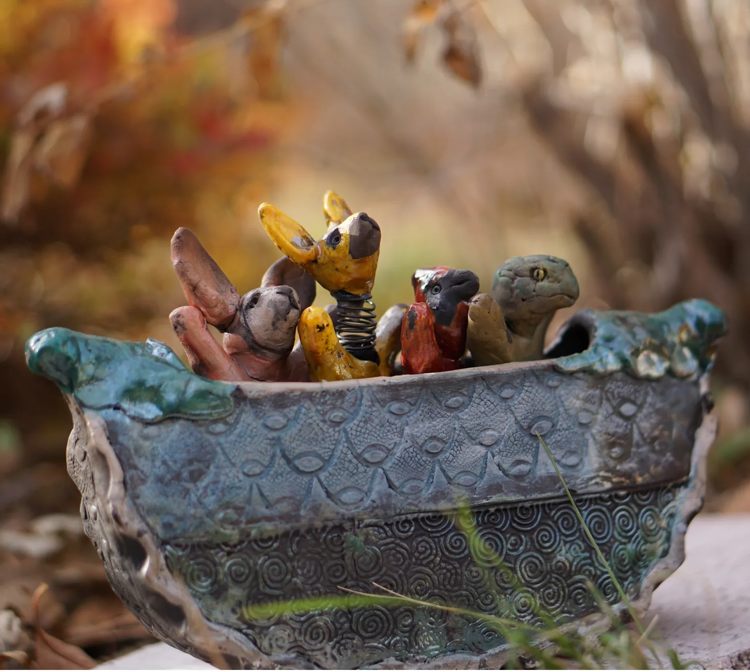 A whimsical ceramic sculpture depicts various animals in a boat, rendered in a folk art style with a textured, earthy palette.