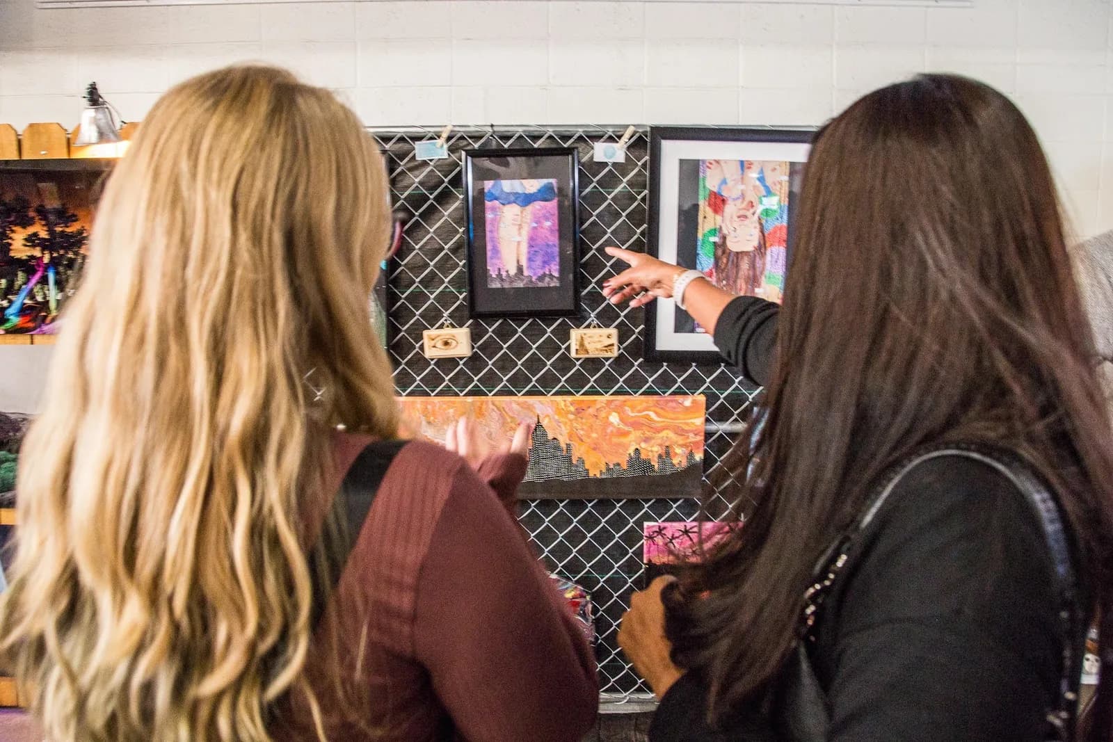 Two people are looking at artwork displayed on a grid wall.