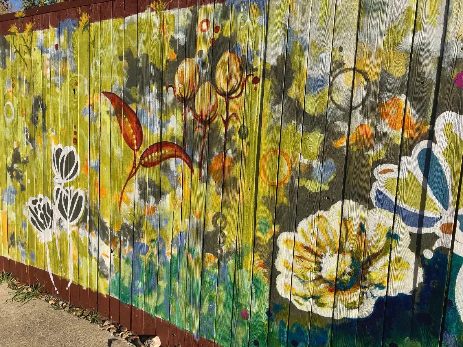 An abstract floral mural painted in Sundance, Roti, and Granite Green hues on a wooden fence.