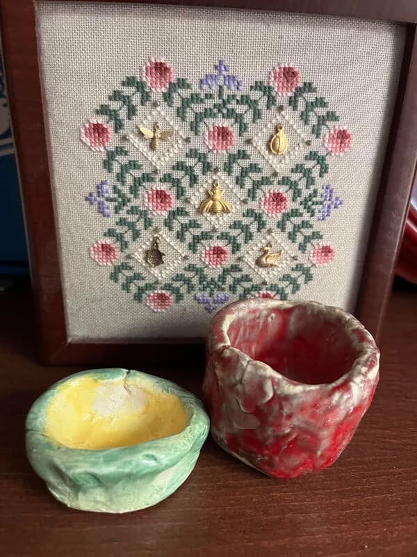 A folk art cross-stitch of floral motifs with embedded charms, featuring bees and swans.