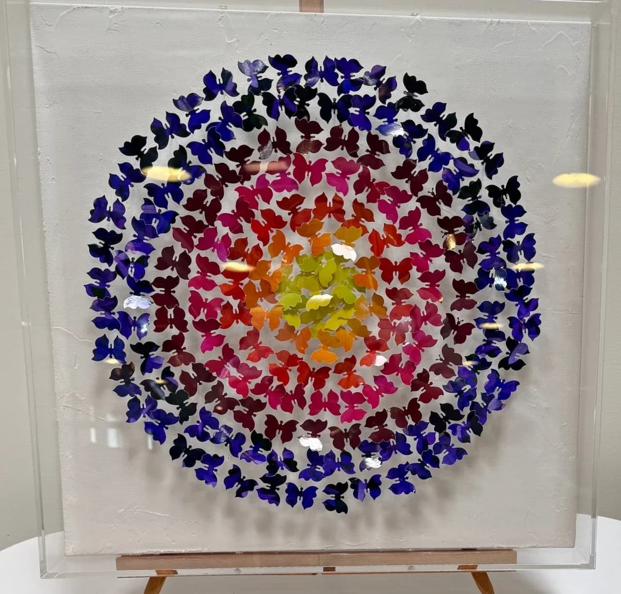A mixed media artwork featuring a mandala of colorful butterflies on a textured white background.