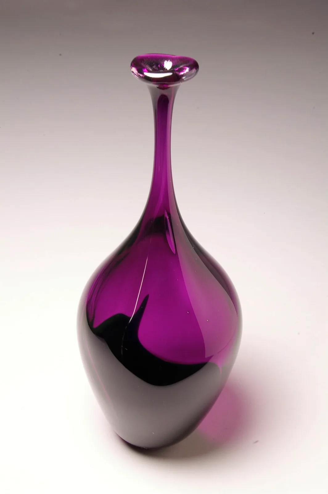 A tall, slender, abstract glass vase in shades of purple and black, with a bulbous base and narrow neck.