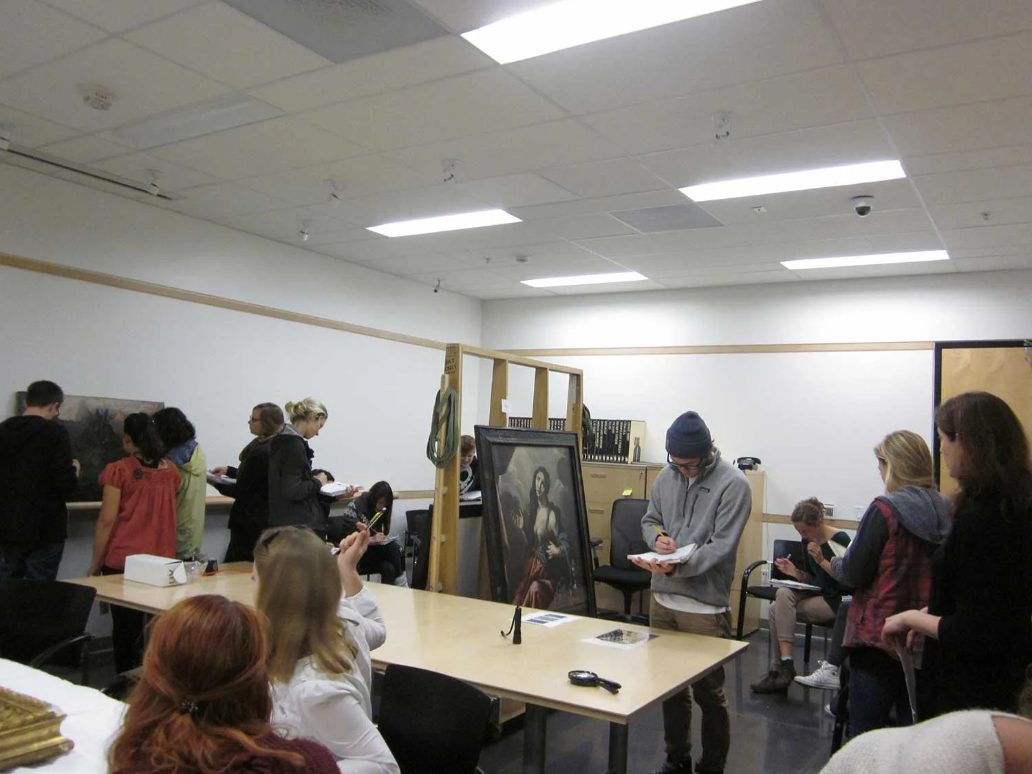 Students observe and sketch a painting in an art classroom setting.