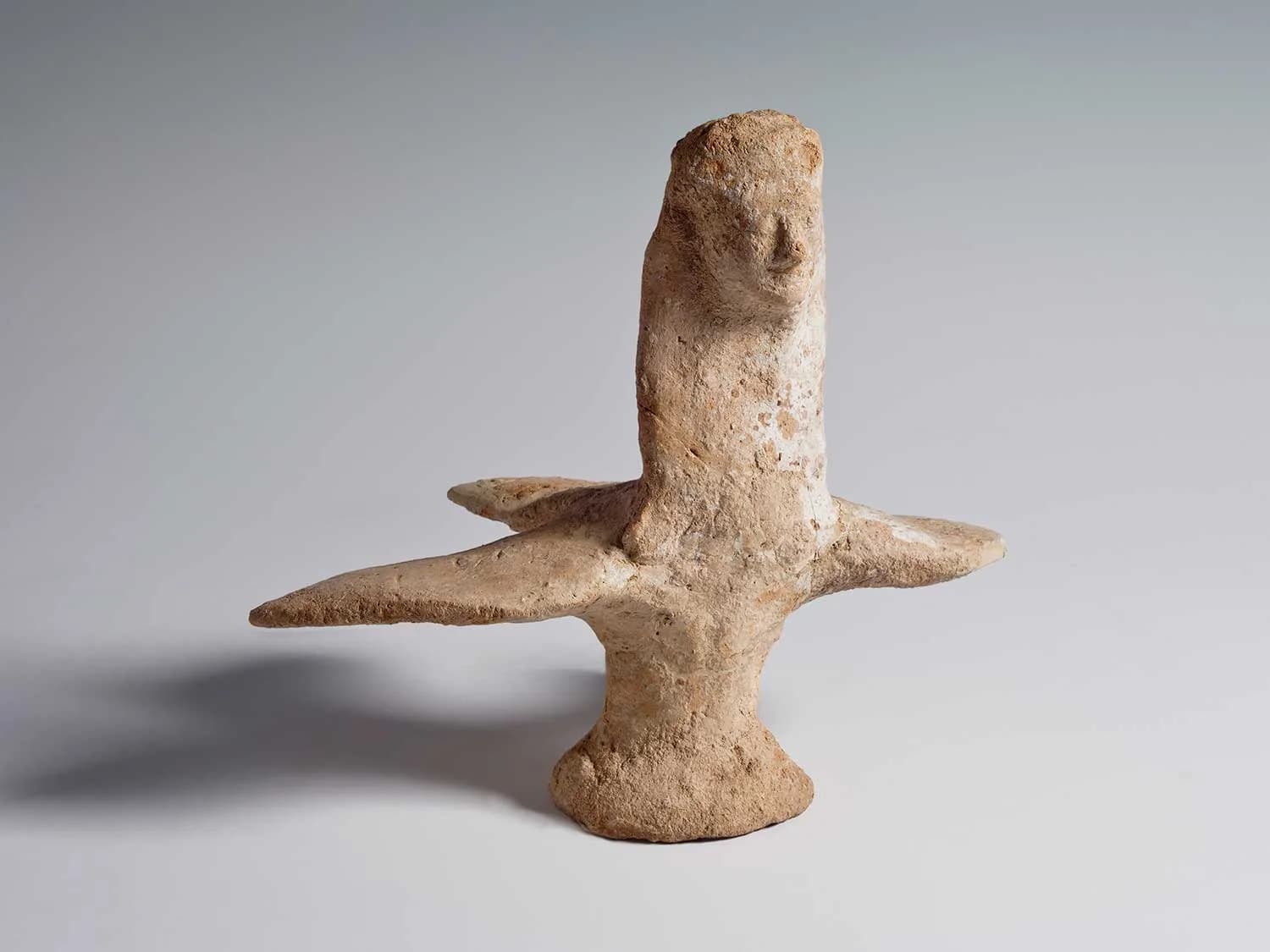 A folk art clay figurine depicts a stylized human figure with outstretched arms, rendered in earthy tones.