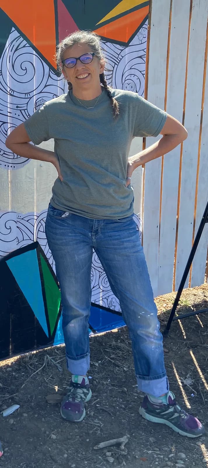 Artist standing in front of a mural in progress, showing colorful geometric shapes and black and white line art.