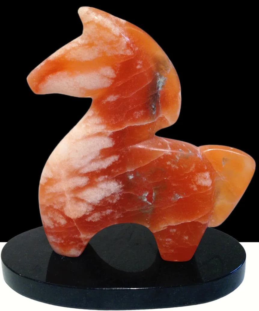 A carved stone horse sculpture in shades of orange and white rests on a black base.