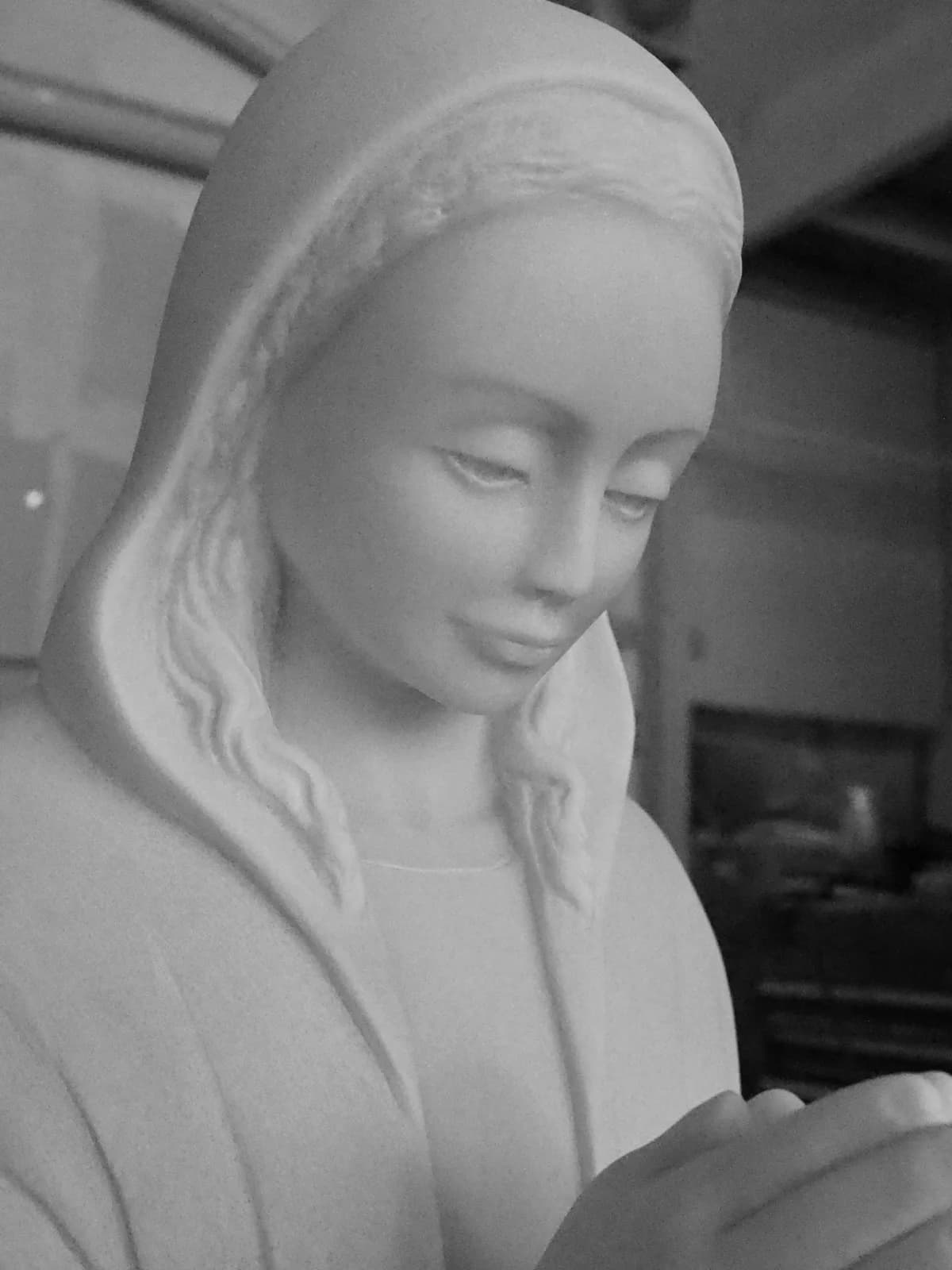 A stone sculpture of a figure in prayer, rendered in shades of gray and white.