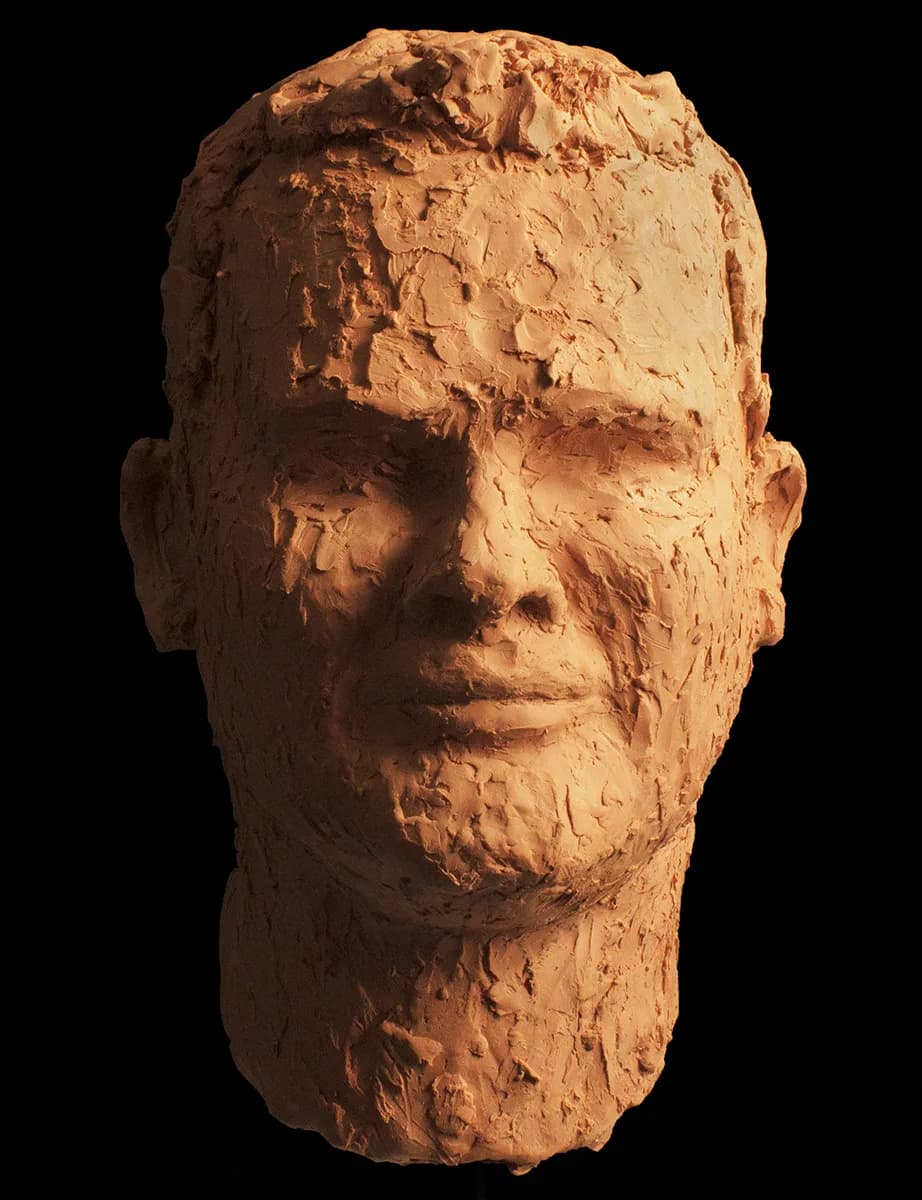 A clay portrait sculpture of a man's head, rendered with textured surfaces and a neutral palette.