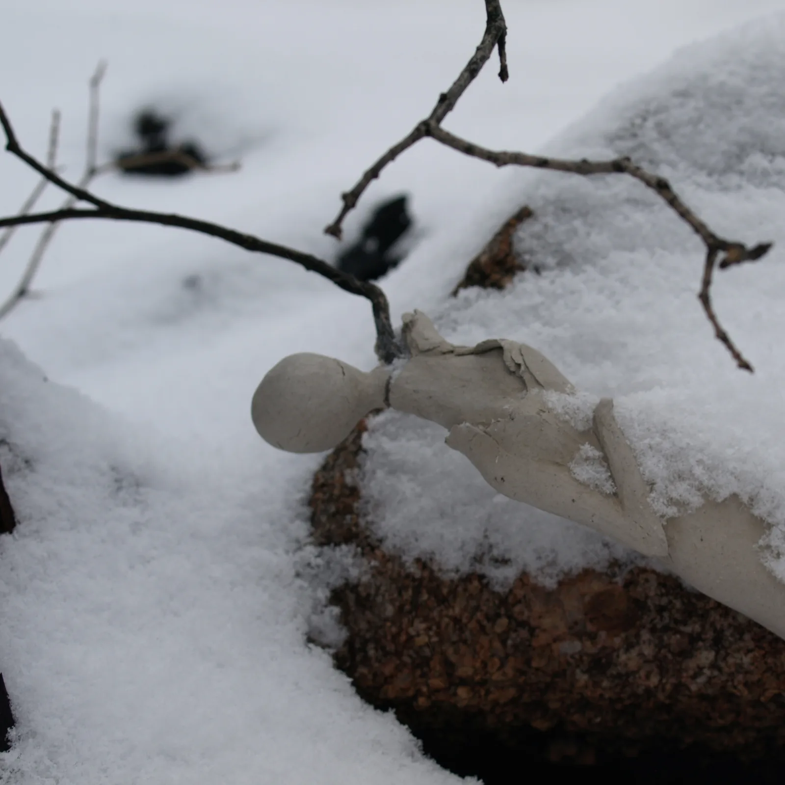 A clay figure sculpture rests in the snow, evoking a sense of winter stillness.