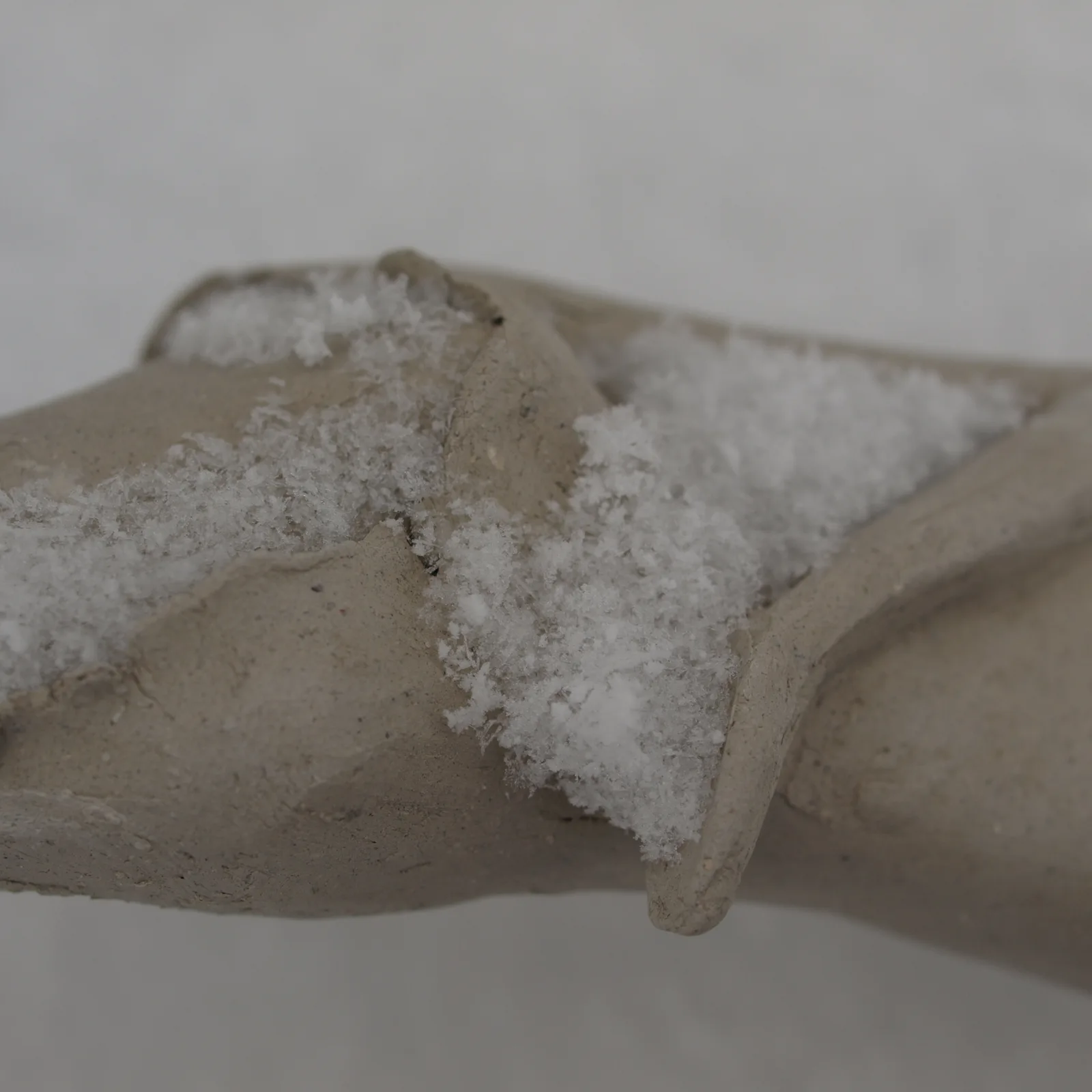 An abstract ceramic sculpture with a textured surface dusted with snow, in shades of Flint and Star Dust.