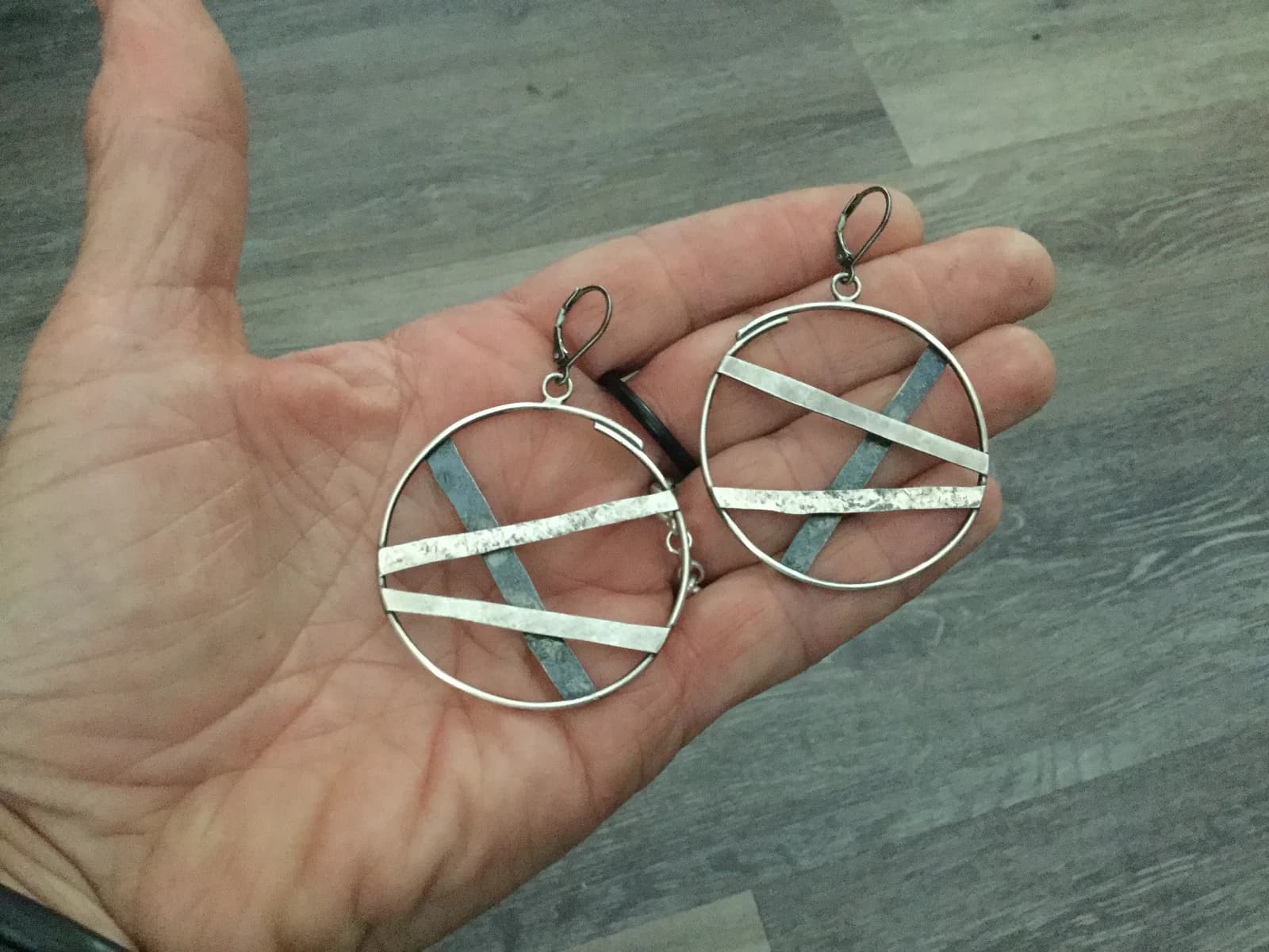 Abstract metal earrings with geometric lines are presented on a hand.