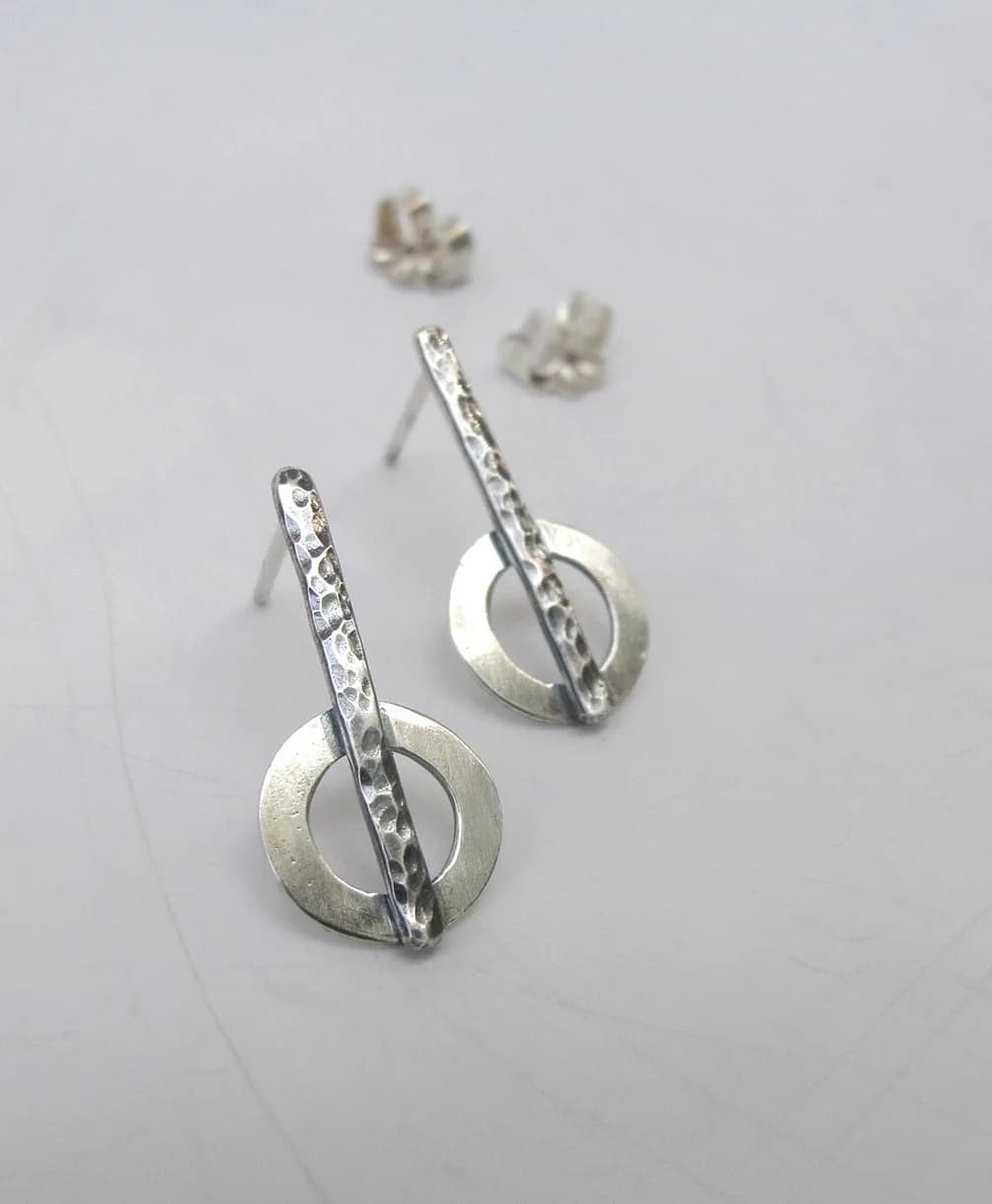 Hammered silver earrings with a geometric design, featuring a bar intersecting a circle.