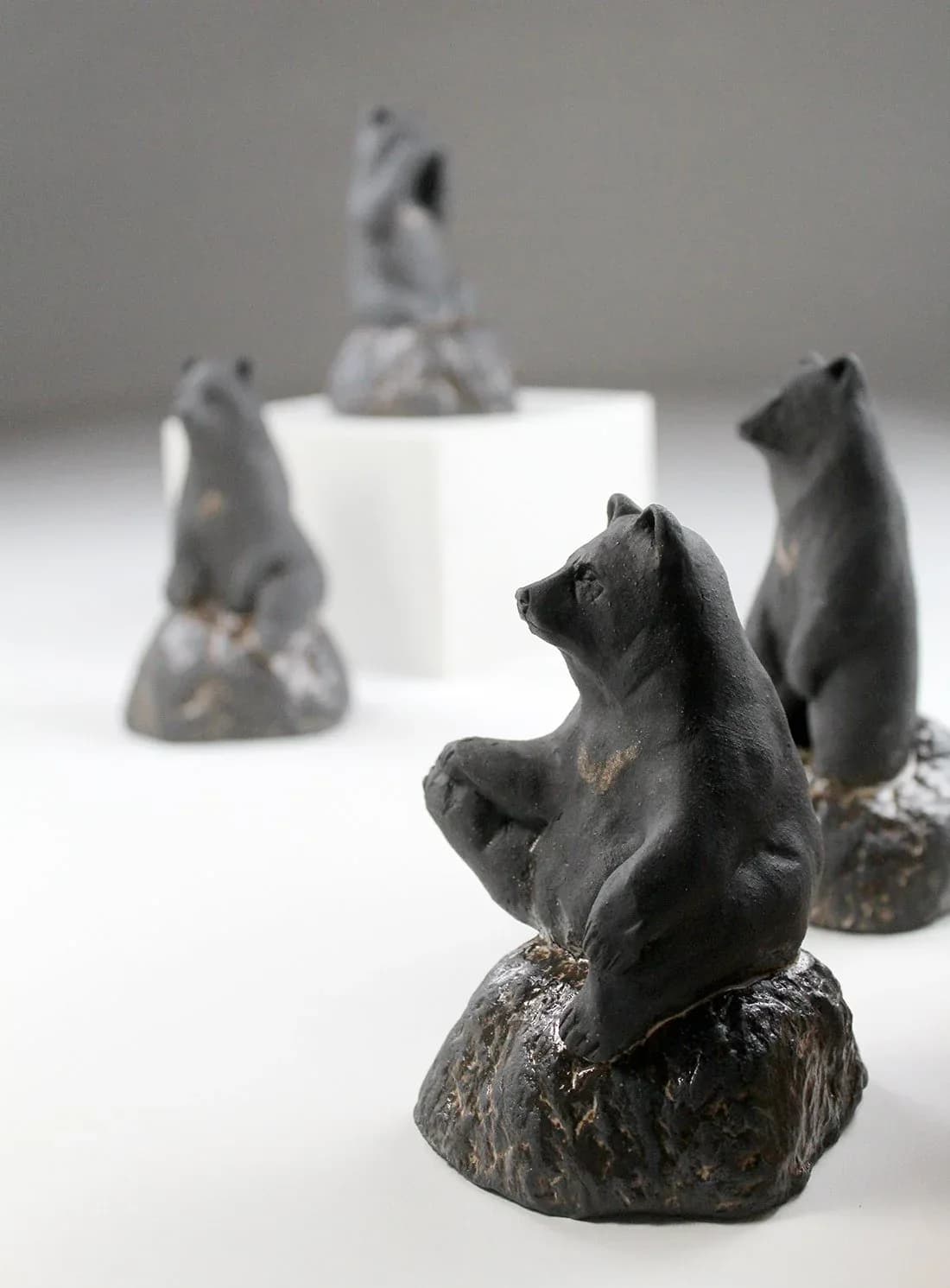 A group of black bear figurines crafted from clay, presented in a neutral studio setting.