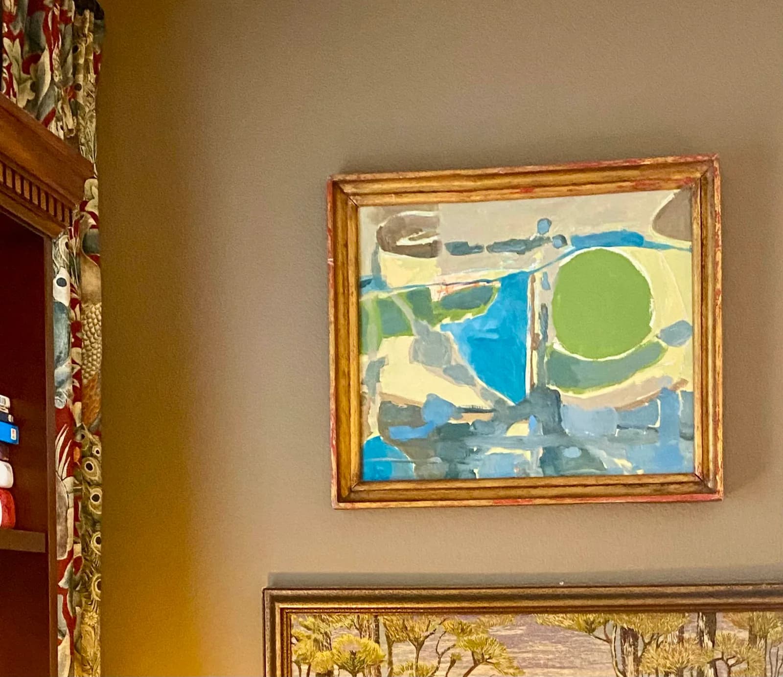 An abstract landscape painting with a prominent green circle hangs on a wall next to a bookshelf.