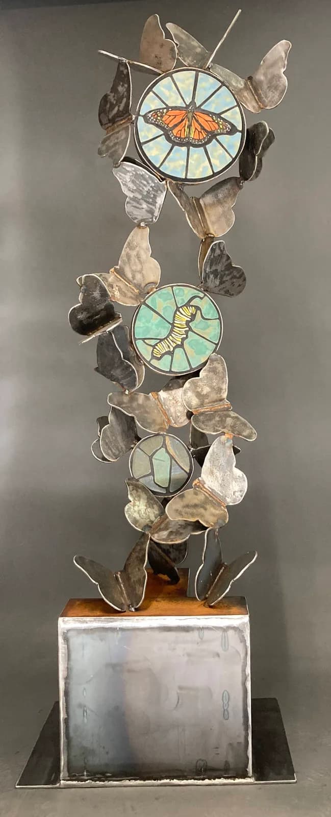 A metal sculpture depicts the life cycle of a monarch butterfly, featuring butterflies and a caterpillar.
