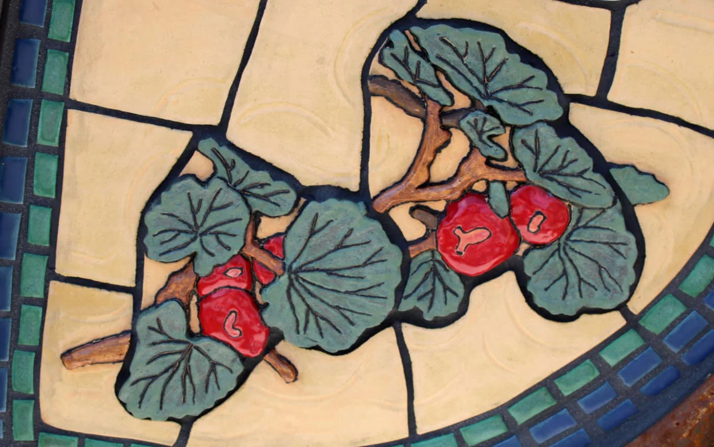 A ceramic tile artwork features red geraniums and green leaves against a cream background, bordered by a mosaic.