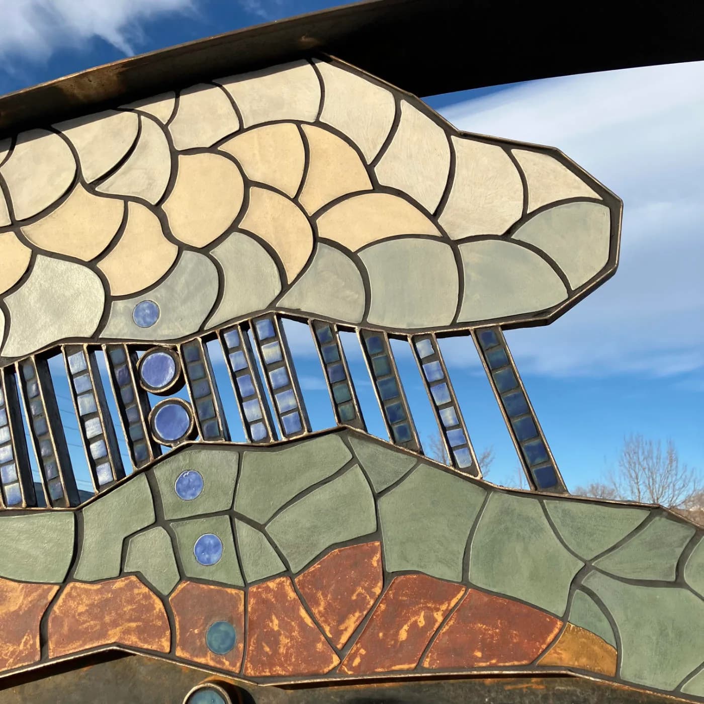 An abstract metal sculpture depicts clouds and rain over a textured landscape in shades of Chamois, Gurkha, and Coffee.