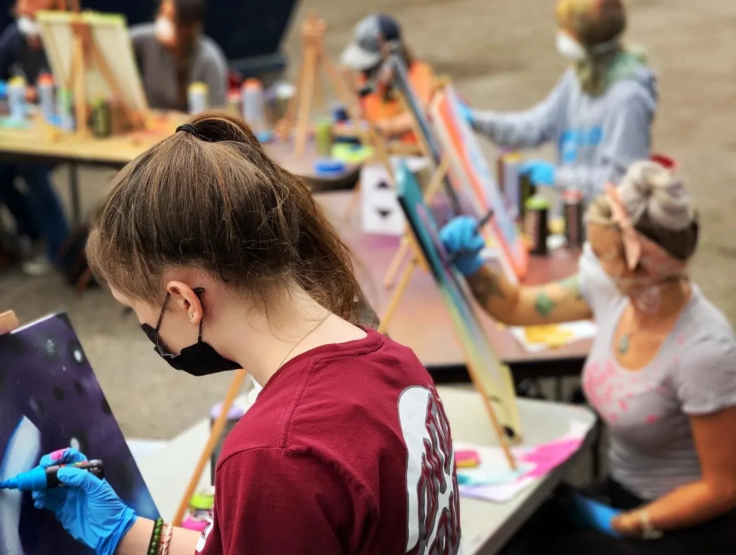 Students participate in an art class, painting on canvases with spray paint and markers.
