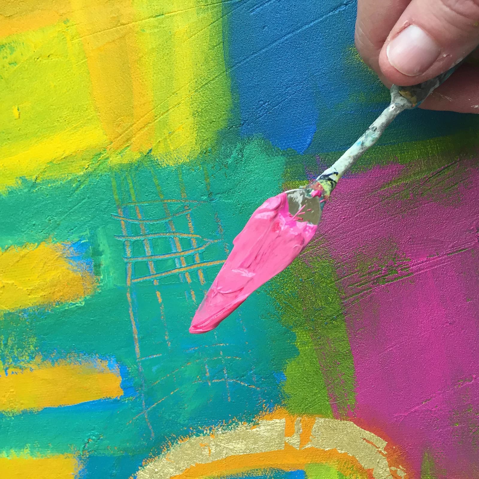 A palette knife with pink paint is held over a vibrant abstract painting in progress.