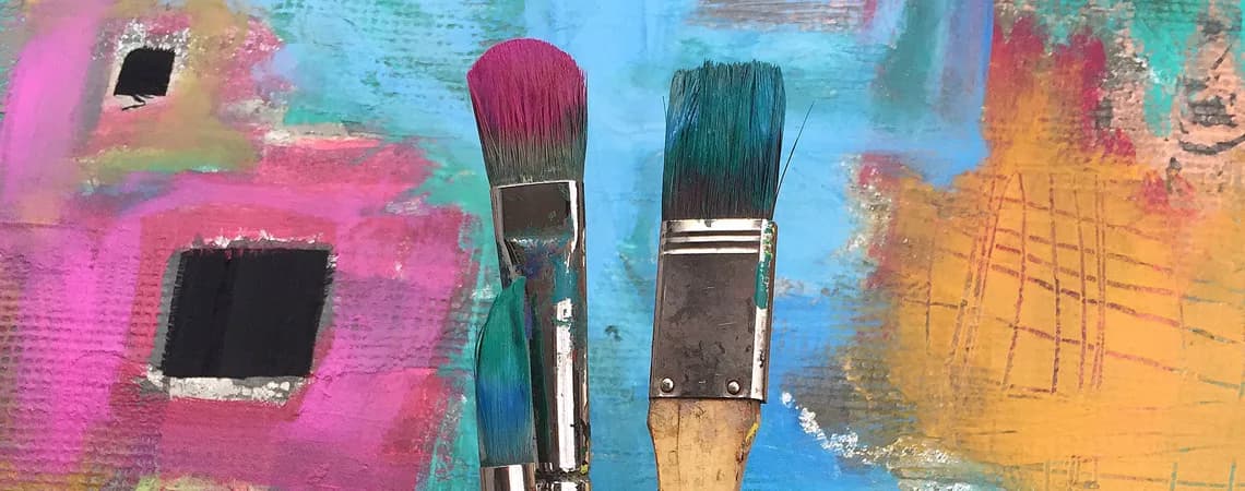 Paintbrushes rest against a vibrant, abstract background with bold pink and blue hues.