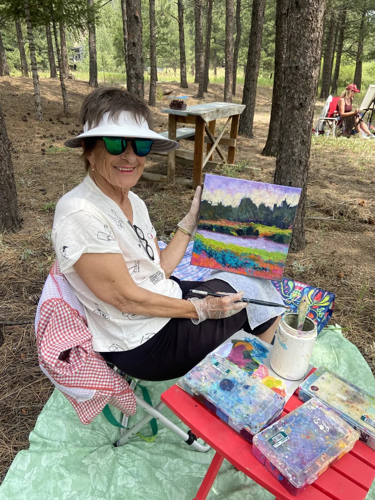 An artist paints a colorful landscape en plein air in a forest setting.
