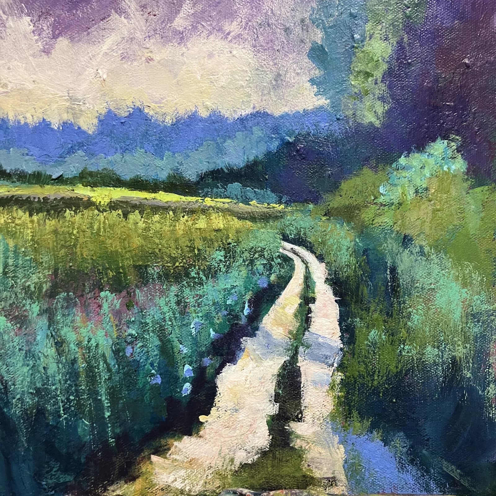 An impressionistic oil painting depicts a winding dirt road through a vibrant meadow with distant mountains under a dramatic sky.