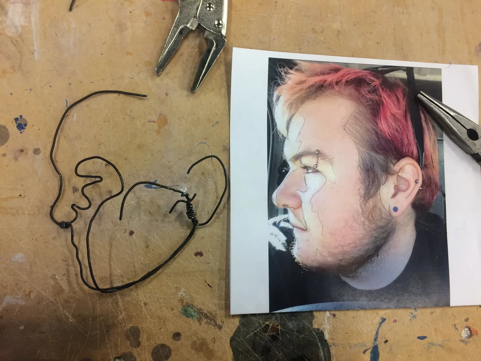 A wire sculpture of a head is shown next to a reference photograph of a person's profile.