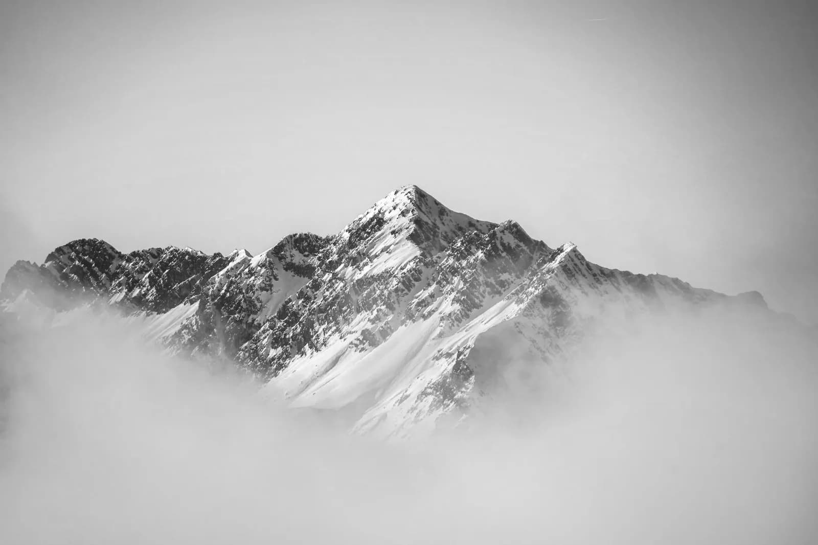 A black and white impressionistic photograph captures a snow-covered mountain peak emerging from mist.