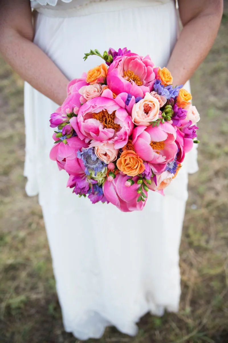 A vibrant floral bouquet of peonies and roses in shades of pink, orange, and purple.