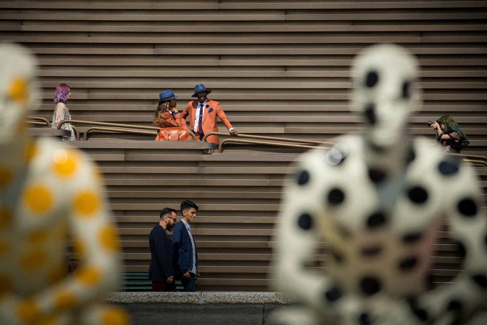 A whimsical polka-dotted sculpture is shown in situ on a tiered outdoor staircase with people in the background.