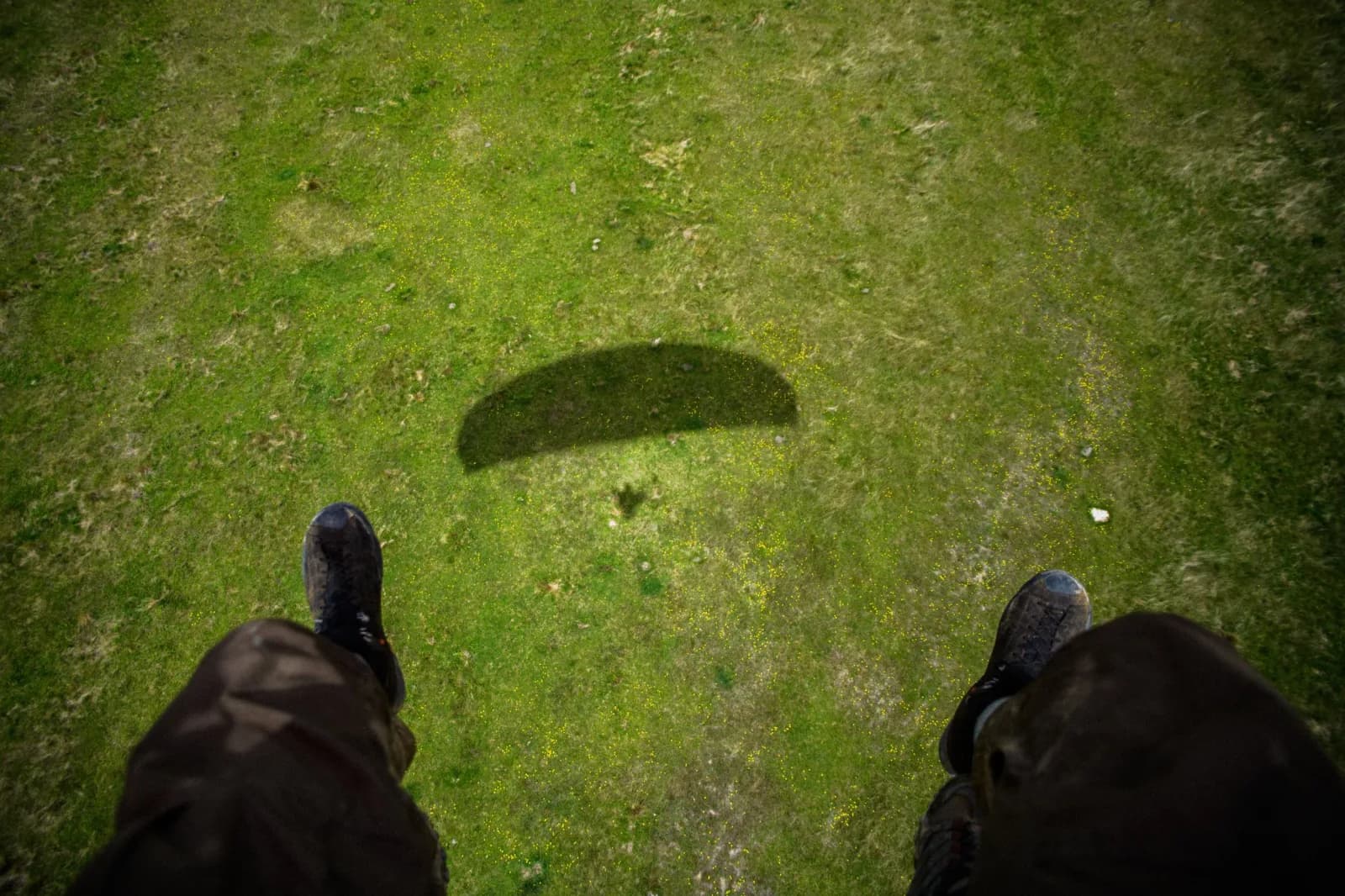 A first-person perspective shot shows a shadow cast on green grass from the viewpoint of someone standing.