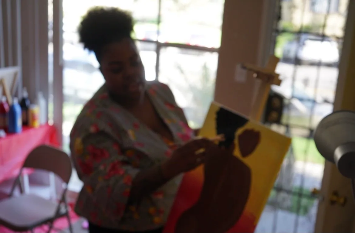 An artist paints a figure on canvas in a furnished studio space.