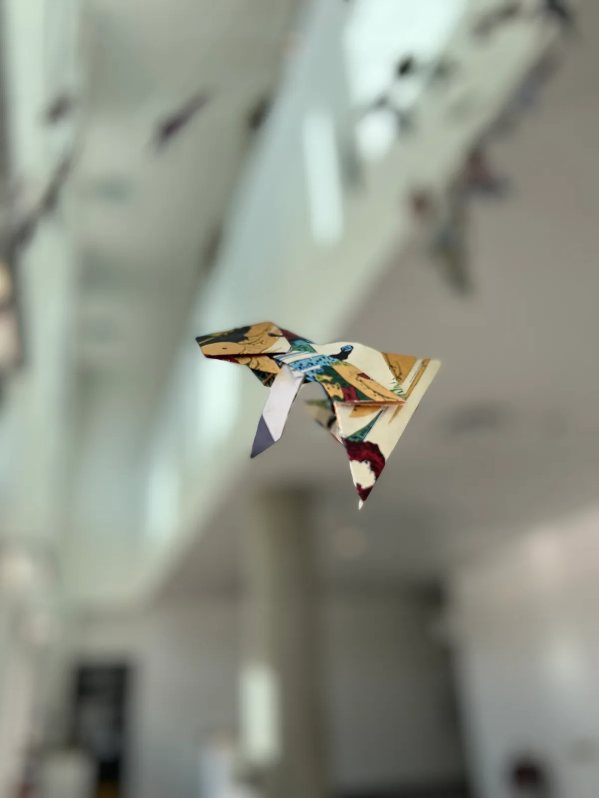 An origami paper crane with a textile pattern, suspended in the air.