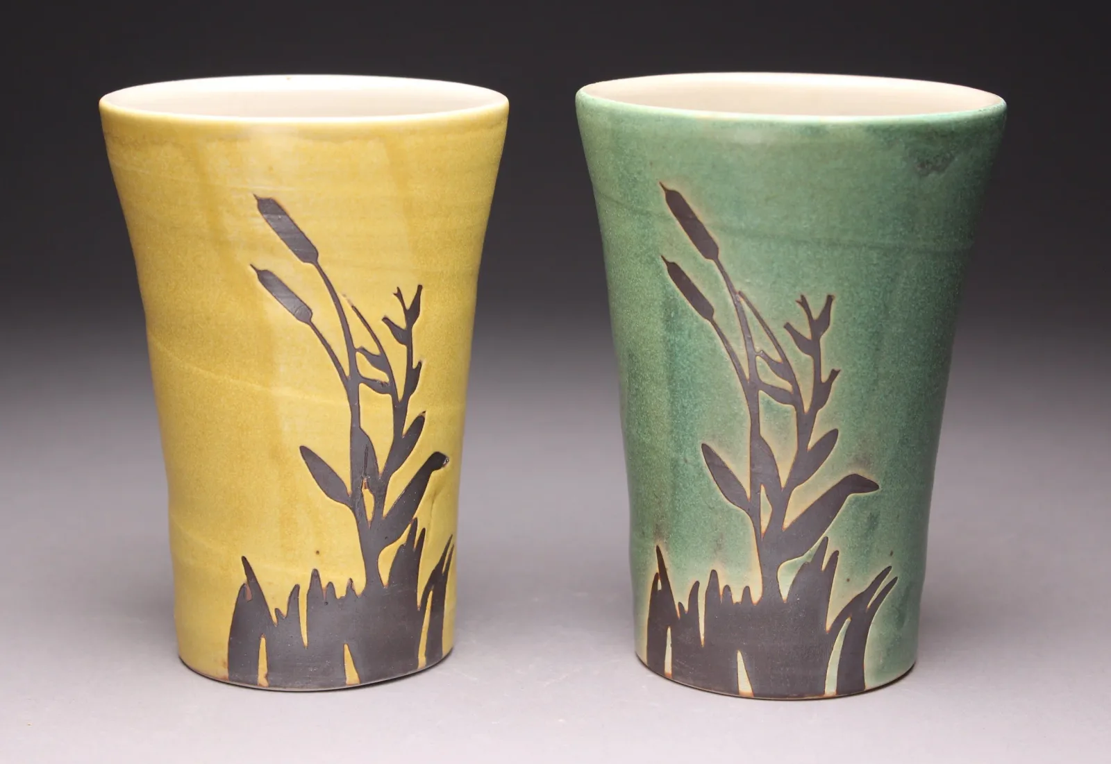 Two ceramic vessels decorated with stylized cattails and grass in a naturalistic palette.