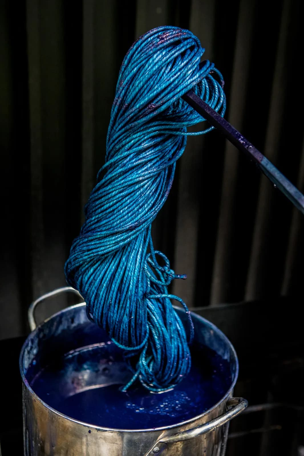 A bundle of blue yarn is being dyed in a vat of dark blue liquid.