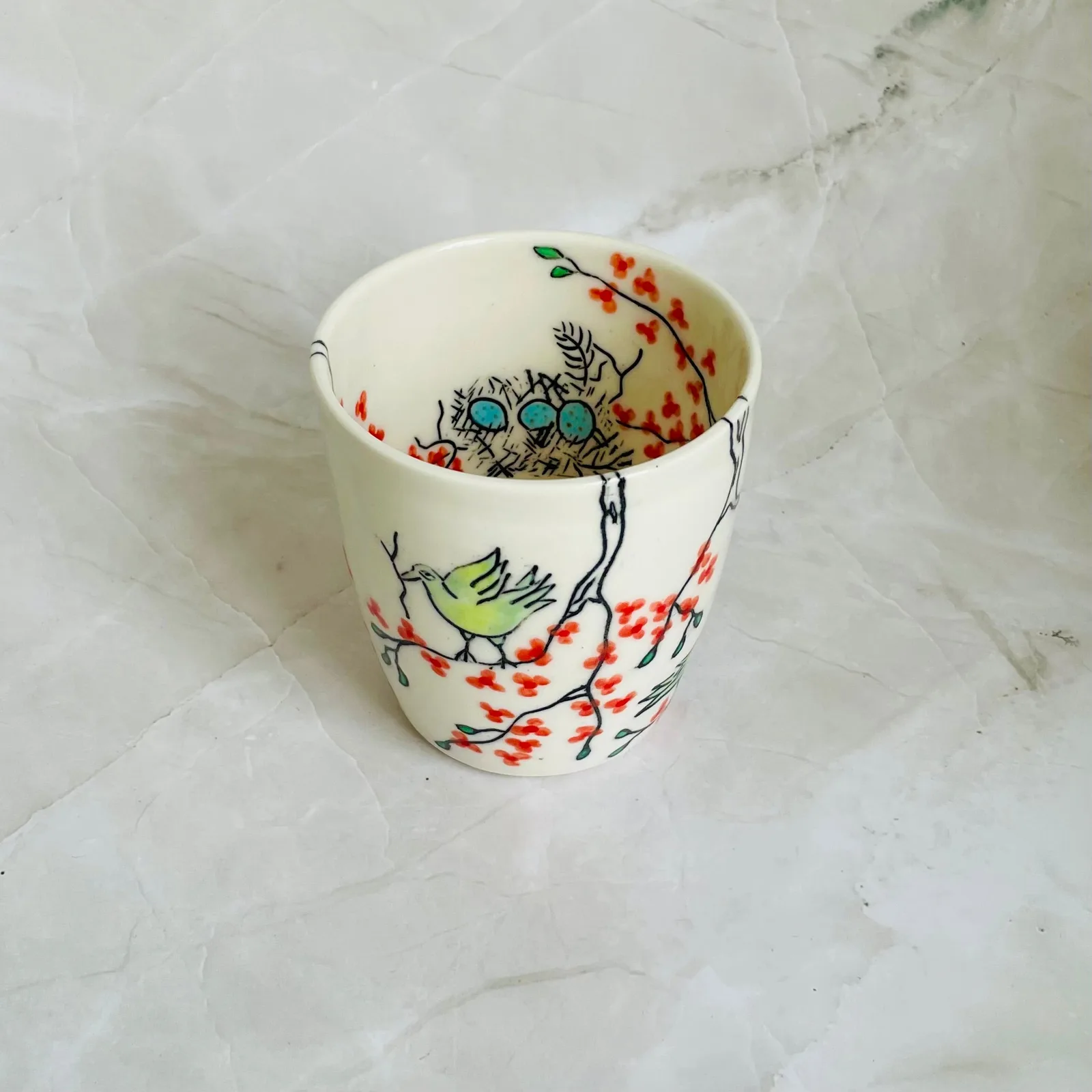 A ceramic cup decorated with a bird, nest, eggs, and blossoms in a folk art style.