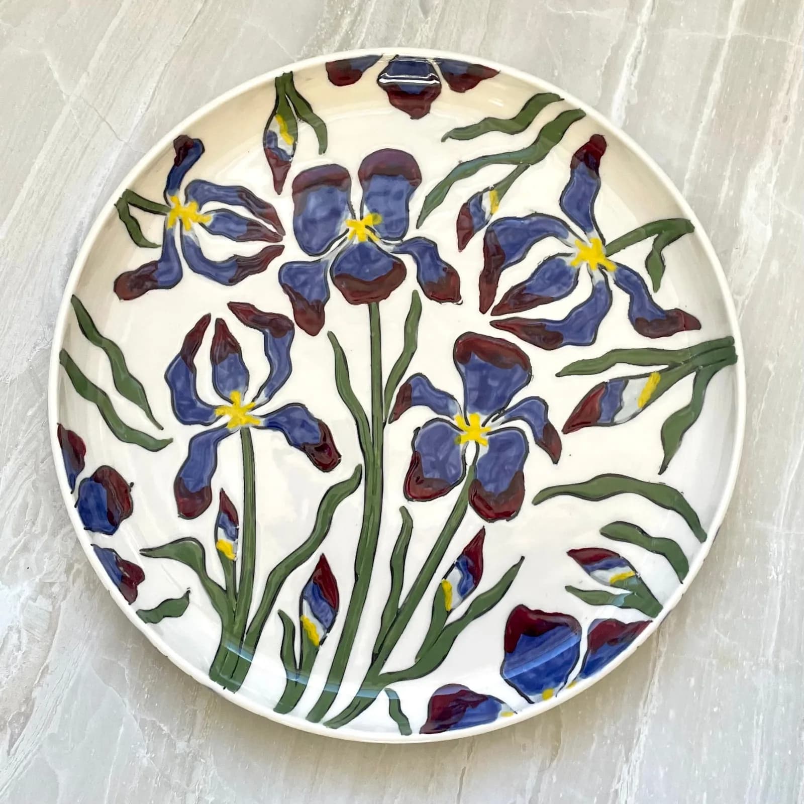 A ceramic plate decorated with blue and maroon irises and green leaves, set against an Ecru White background.