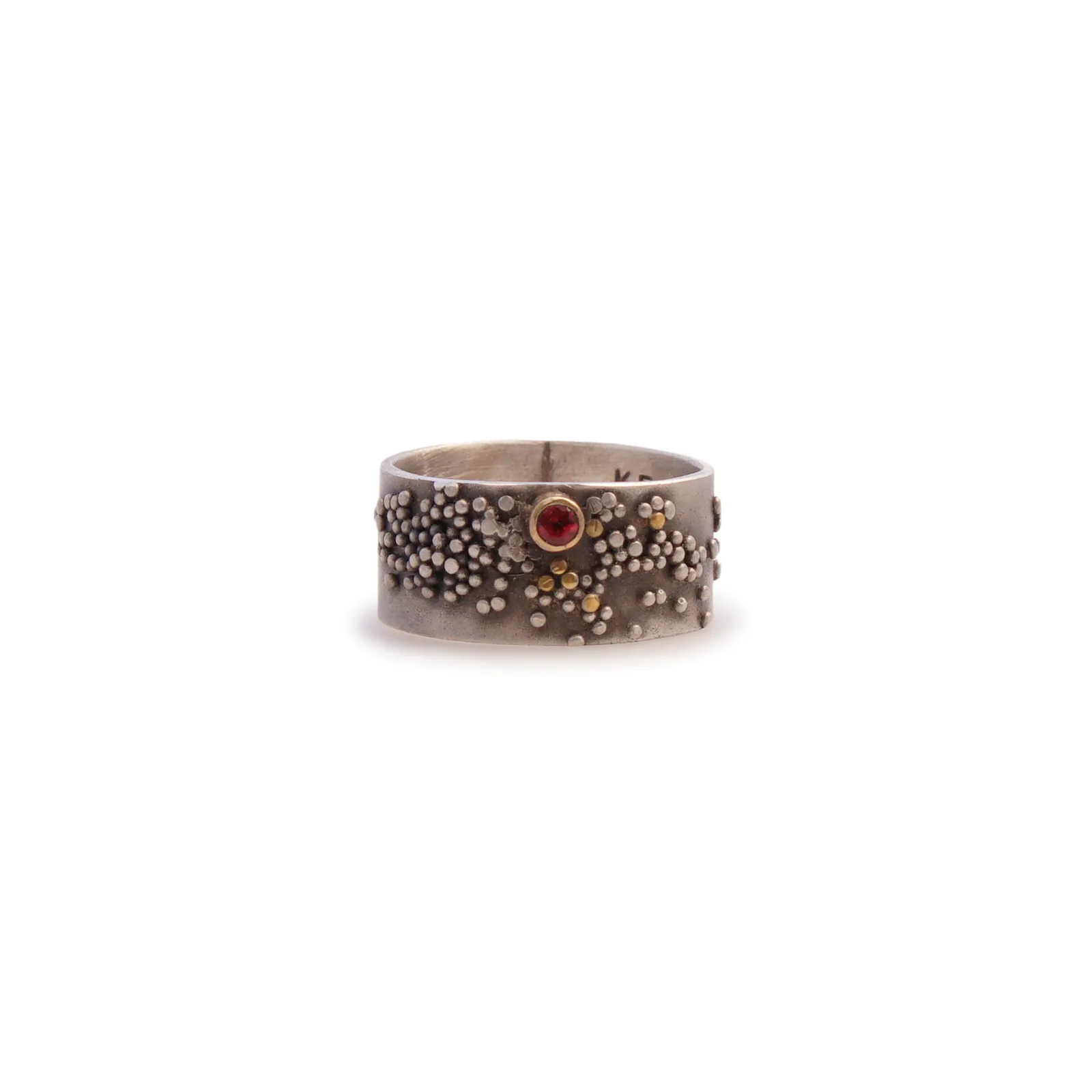 A textured metal ring with a central red gemstone and scattered gold accents.