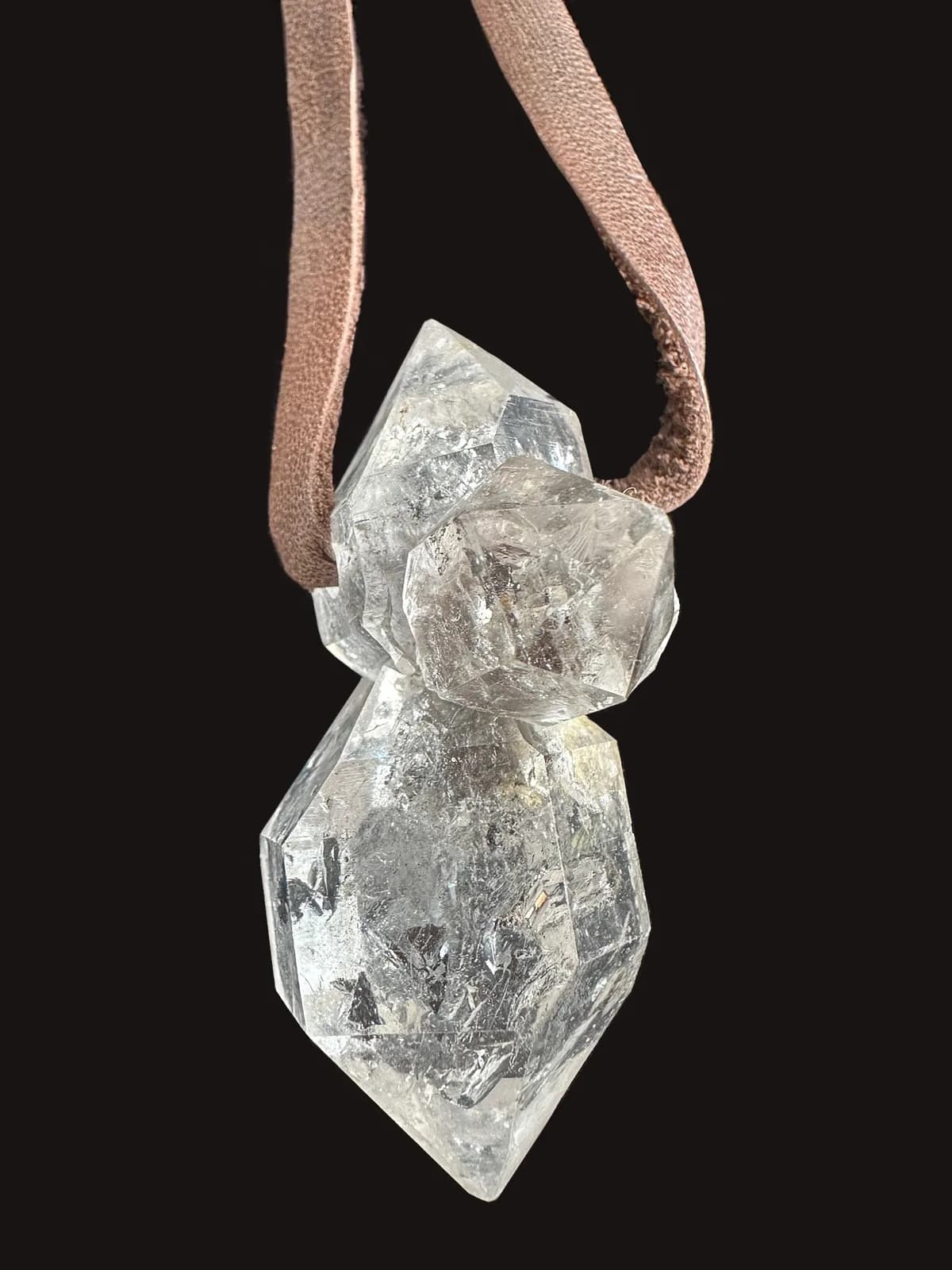 A clear quartz crystal pendant hangs from a leather cord, showcasing its natural facets and inclusions.
